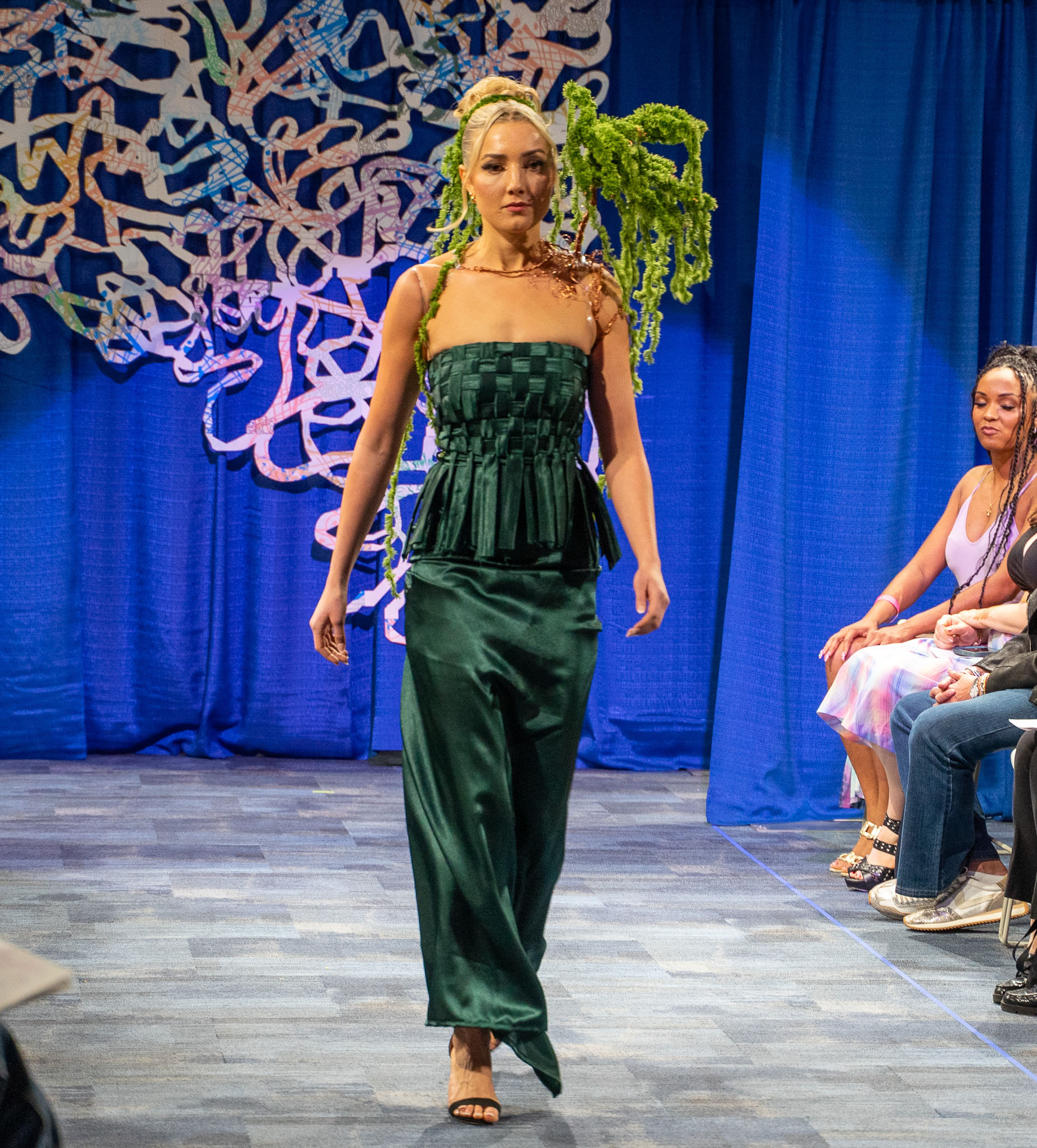 Student model in green dress walking down runway