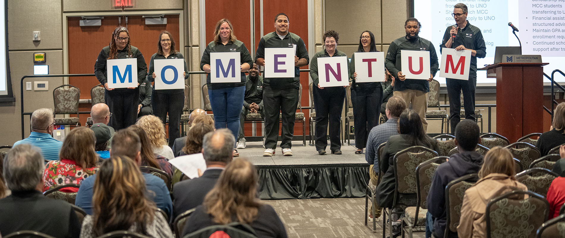 Group of people holding letter sing that spells out momentum