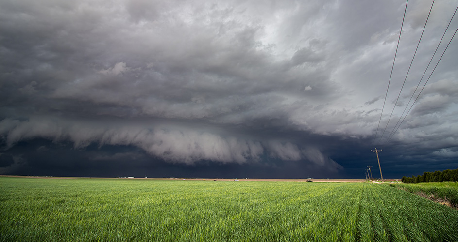 An ominous gray storm cloud rolls in over a farm field