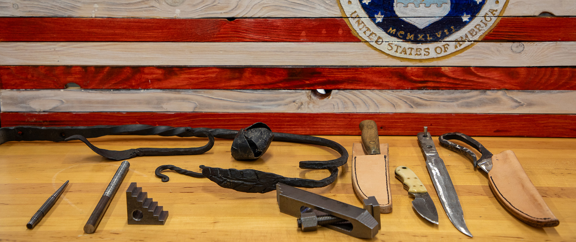 Knives, hooks and other blacksmithing projects Talkington has completed displayed in front of a wooden American flag honoring the U.S. Air Force