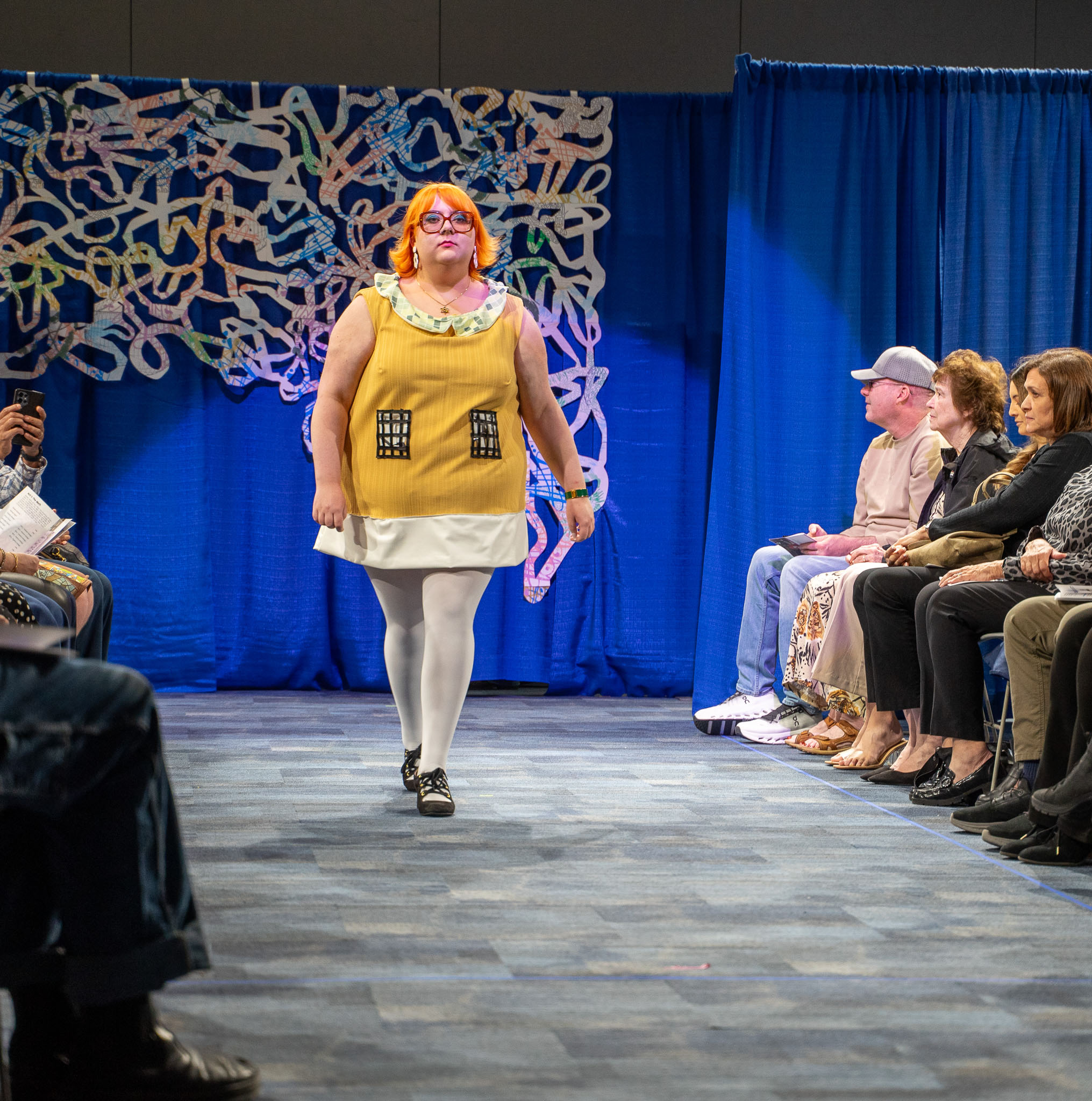 Student model in yellow dress walking down runway
