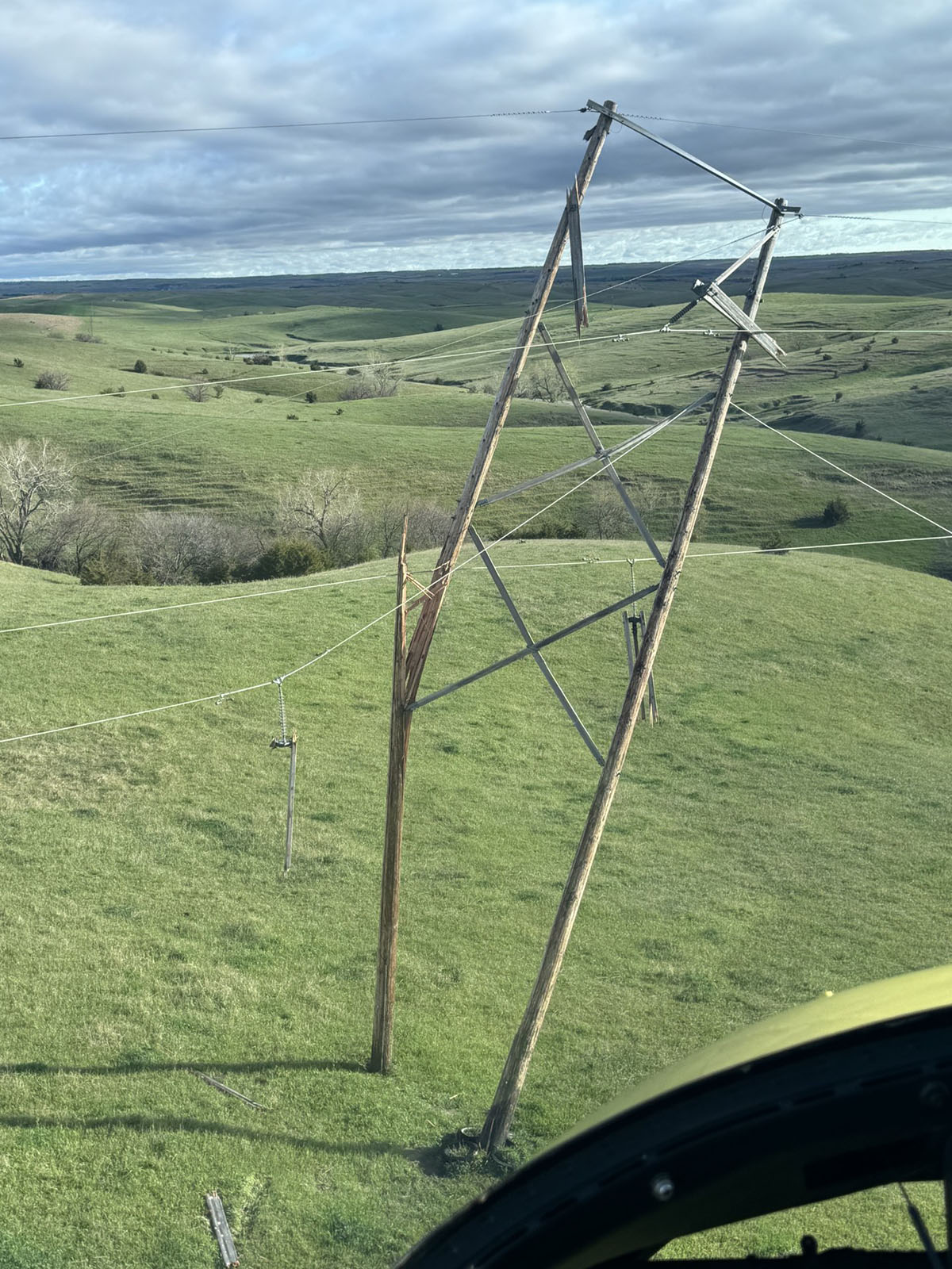 A snapped utility line pole damaged by severe weather dangles over a field