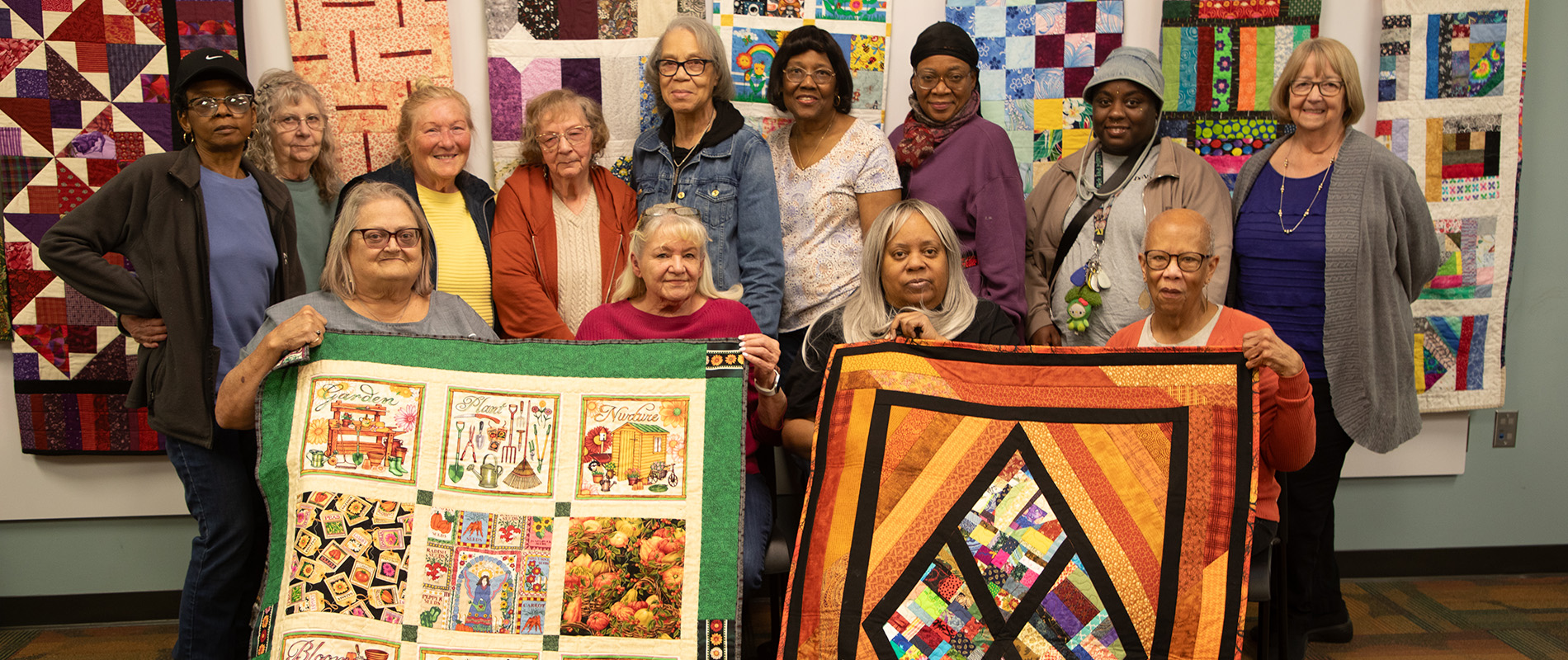 A group photo of members of Quilters We Are displaying finished quilts