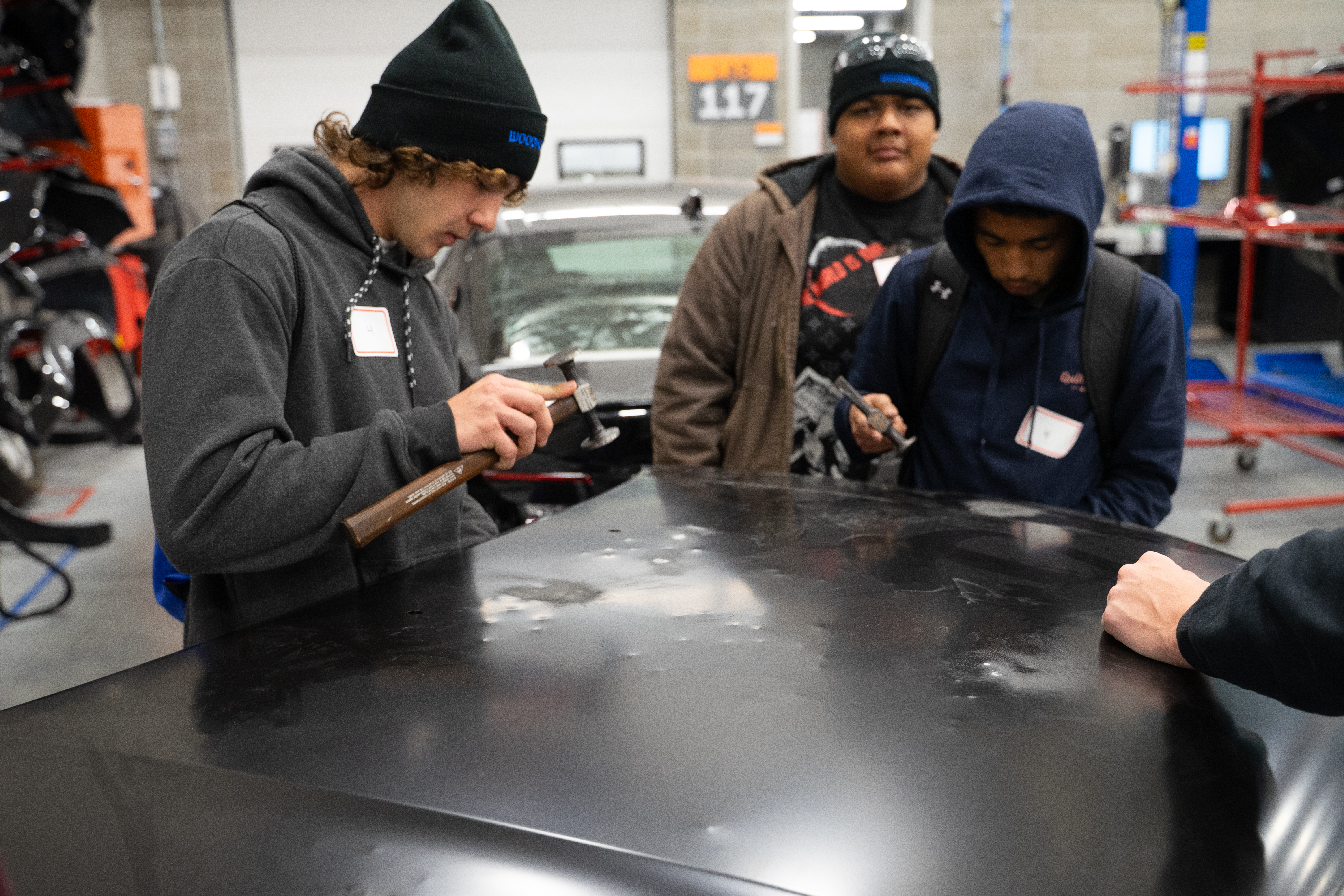 Students practice working with automotive body repair tools.